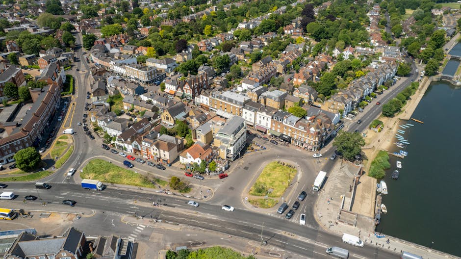A street scene in Kingston with several parked and moving cars along a paved road, lined by mature trees casting shade over the pavement. In the background, there is a historic church building featuri